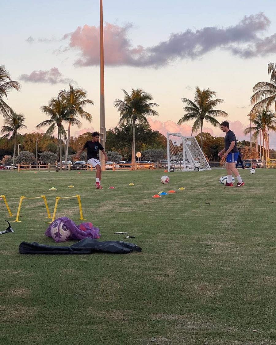 Young athlete striking the ball through a cone gate while Coach Austin watches